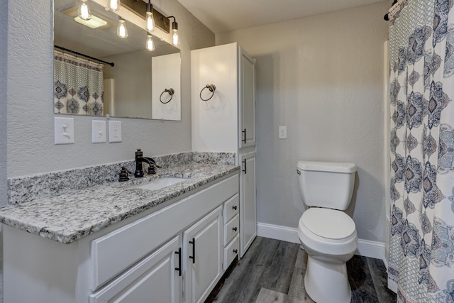 full bathroom with wood finished floors, toilet, vanity, baseboards, and a textured wall