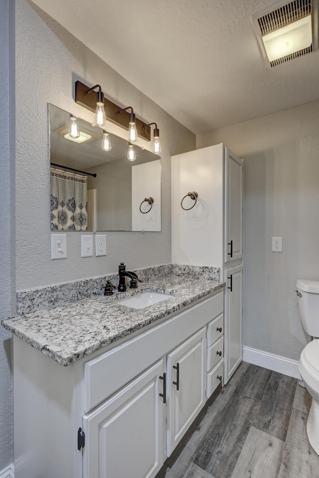 bathroom with wood finished floors, toilet, a textured wall, vanity, and a textured ceiling