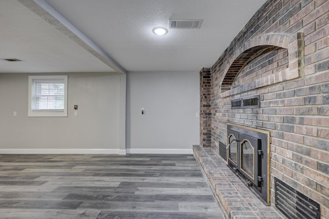 unfurnished living room with a brick fireplace, brick wall, a textured ceiling, baseboards, and wood finished floors