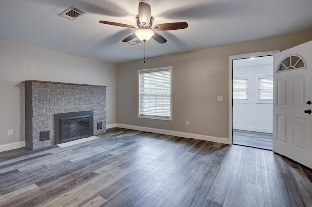 unfurnished living room with a ceiling fan, healthy amount of natural light, a fireplace, and dark wood finished floors