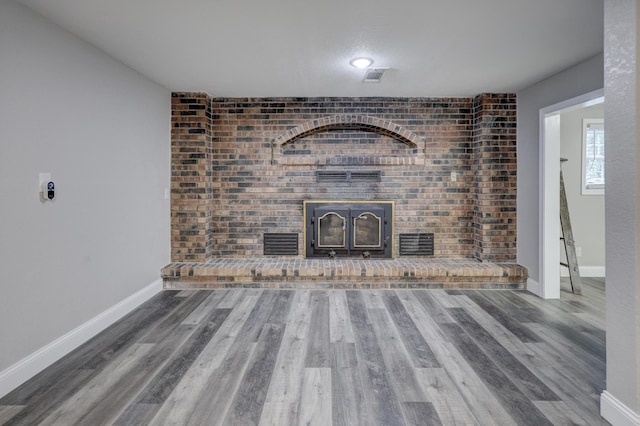 unfurnished living room featuring a brick fireplace, wood finished floors, baseboards, and brick wall