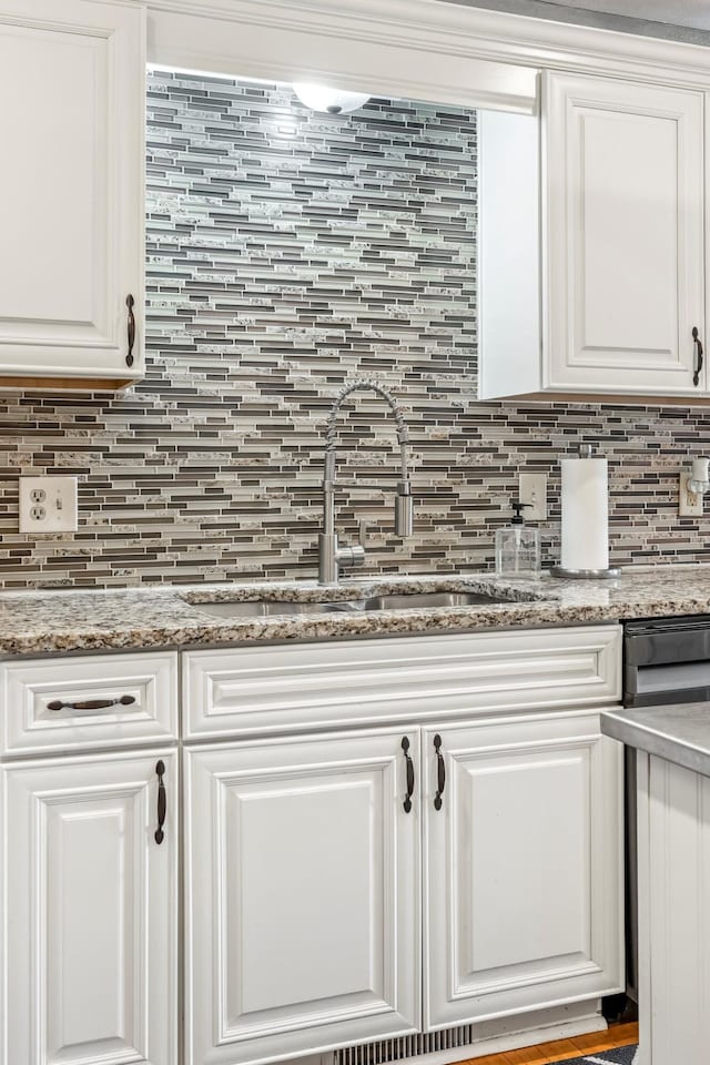 kitchen view of a sink, tasteful backsplash, white cabinetry, and light stone counters