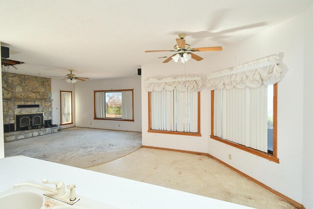 unfurnished living room with ceiling fan, a stone fireplace, and baseboards