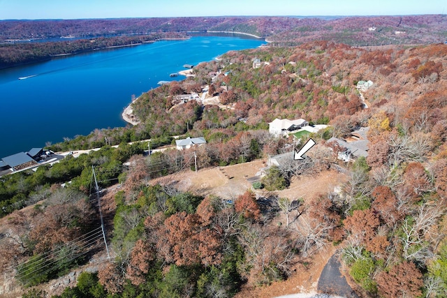 aerial view of property and surrounding area featuring a nearby body of water and a heavily wooded area