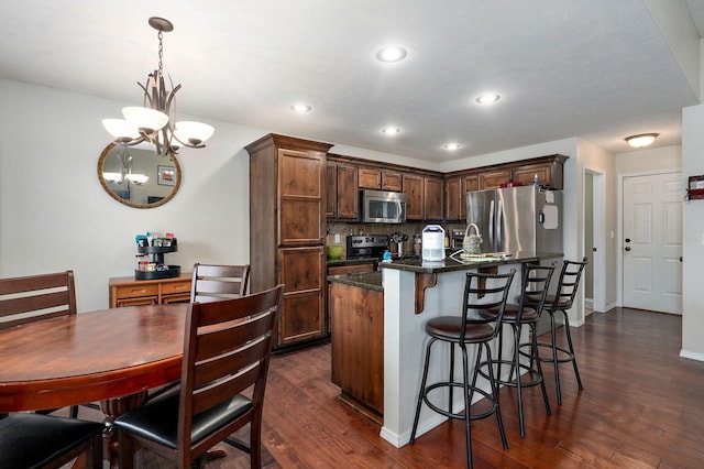 kitchen with appliances with stainless steel finishes, dark wood finished floors, a kitchen bar, a chandelier, and backsplash