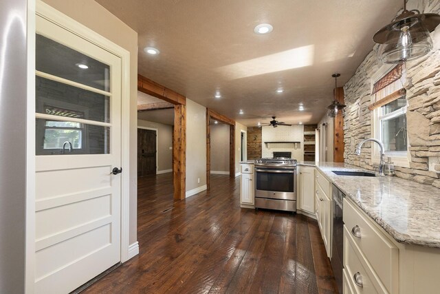 kitchen featuring appliances with stainless steel finishes, a sink, a large fireplace, dark wood-style flooring, and light stone countertops