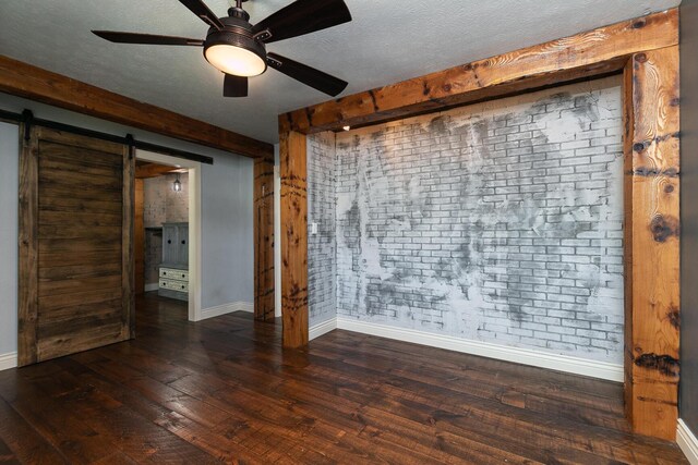 spare room with baseboards, a barn door, a ceiling fan, wood-type flooring, and a textured ceiling