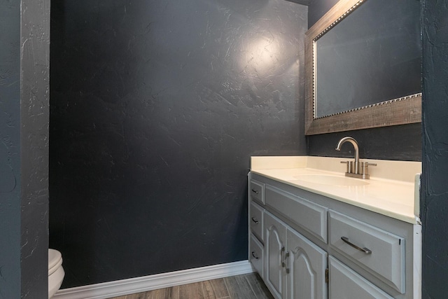 half bathroom with wood finished floors, toilet, vanity, and baseboards