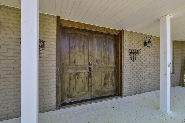 view of exterior entry with brick siding and a porch