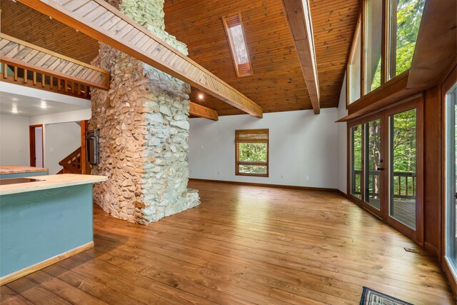 unfurnished living room with high vaulted ceiling, hardwood / wood-style floors, baseboards, beamed ceiling, and a skylight