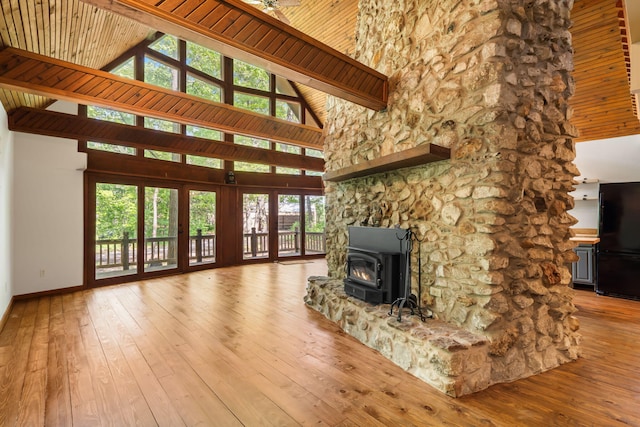 unfurnished living room featuring high vaulted ceiling, baseboards, hardwood / wood-style flooring, french doors, and a wood stove