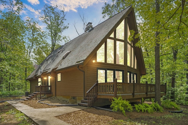 view of property exterior featuring a chimney, a deck, roof with shingles, and central air condition unit