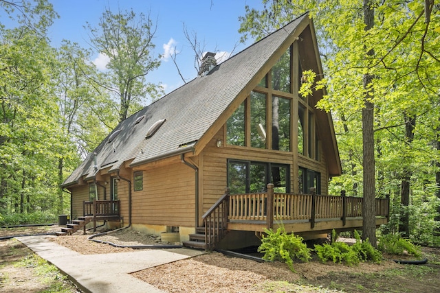 rear view of property featuring a chimney, roof with shingles, a wooden deck, and central AC