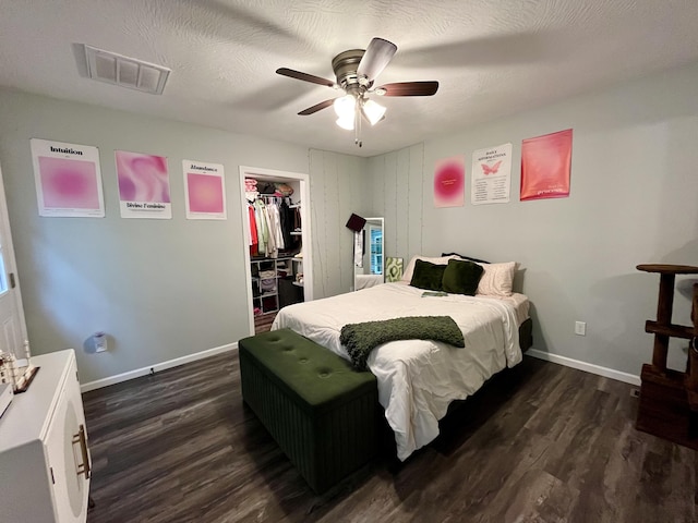 bedroom featuring dark wood-style flooring, baseboards, a walk in closet, ceiling fan, and a closet