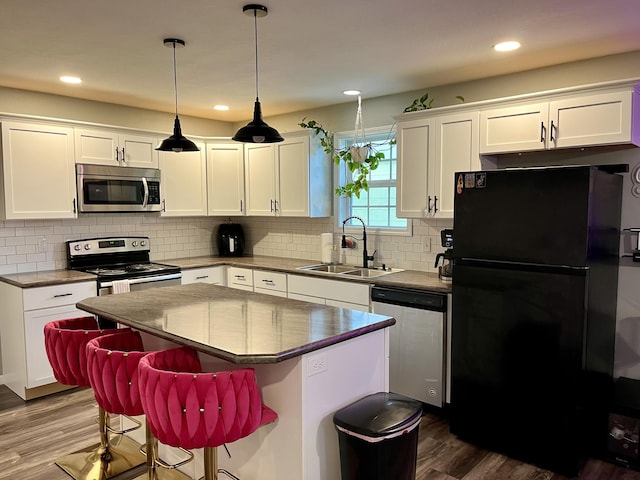 kitchen with appliances with stainless steel finishes, a sink, dark wood-style floors, white cabinets, and a center island