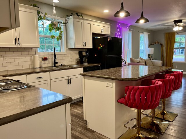 kitchen with open floor plan, freestanding refrigerator, dark countertops, a center island, and white cabinetry