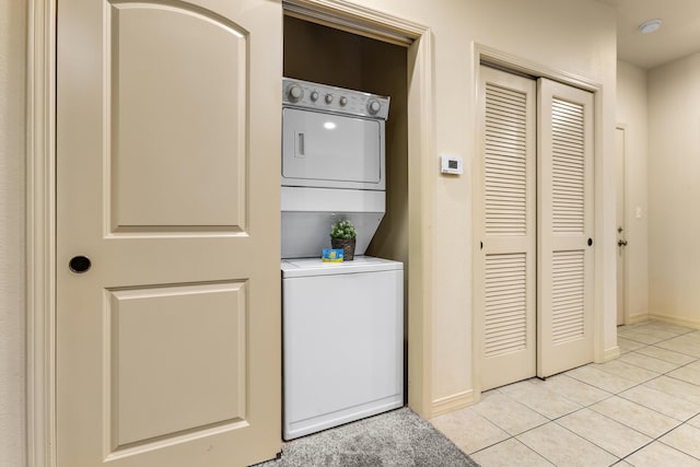 laundry area featuring stacked washing machine and dryer, light tile patterned floors, and baseboards