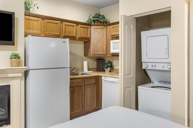 kitchen with white appliances, estacked washer and dryer, brown cabinetry, light countertops, and a sink