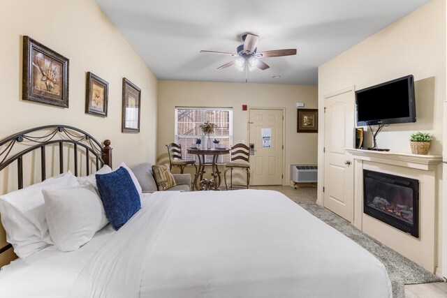 carpeted bedroom featuring a glass covered fireplace, a wall unit AC, and a ceiling fan