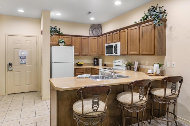 kitchen featuring white appliances, light countertops, a peninsula, brown cabinets, and recessed lighting