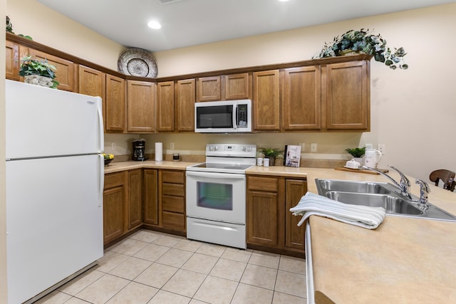 kitchen with white appliances, a sink, brown cabinets, light countertops, and light tile patterned flooring