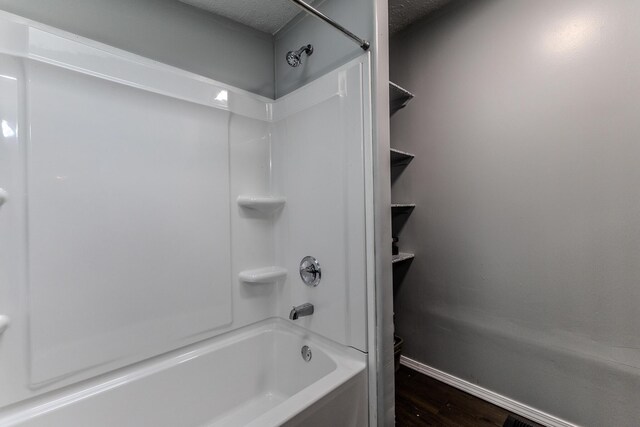 full bath featuring wood finished floors, baseboards, shower / tub combination, and a textured ceiling