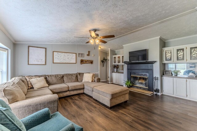 living room featuring a textured ceiling, dark wood-type flooring, ceiling fan, a glass covered fireplace, and ornamental molding
