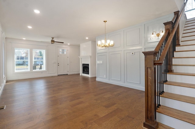 unfurnished living room with recessed lighting, stairs, a ceiling fan, dark wood finished floors, and a chandelier