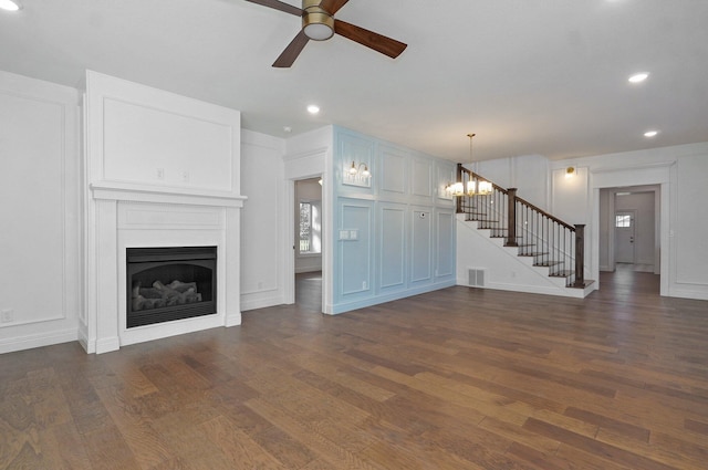 unfurnished living room with stairway, ceiling fan, dark wood-style flooring, a fireplace, and a decorative wall