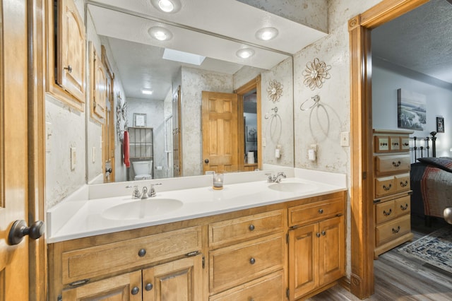5425 S Westwood Ave, Springfield, MO 65810 - ensuite bathroom featuring wood finished floors, wallpapered walls, toilet, double vanity, and a skylight