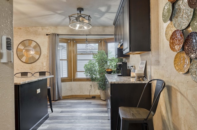 5425 S Westwood Ave, Springfield, MO 65810 - kitchen featuring light wood-type flooring, light stone counters, a textured wall, baseboards, and decorative light fixtures