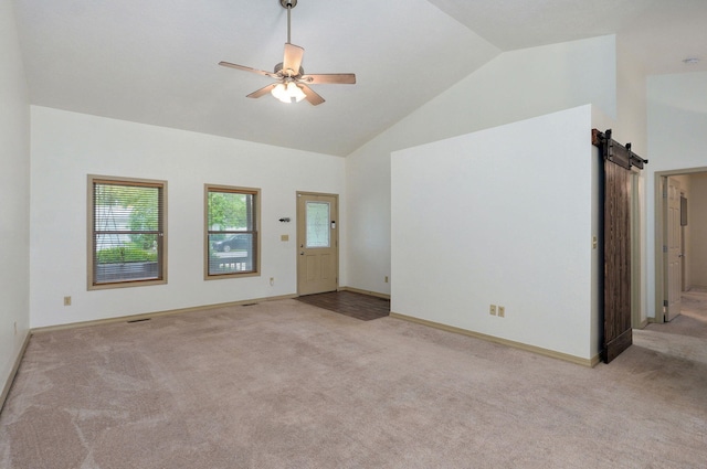 unfurnished living room with light carpet, a barn door, a ceiling fan, baseboards, and high vaulted ceiling