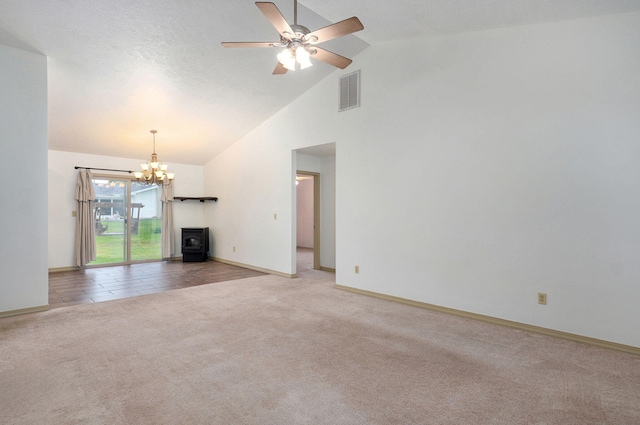 unfurnished living room featuring a wood stove, light carpet, high vaulted ceiling, a chandelier, and a ceiling fan
