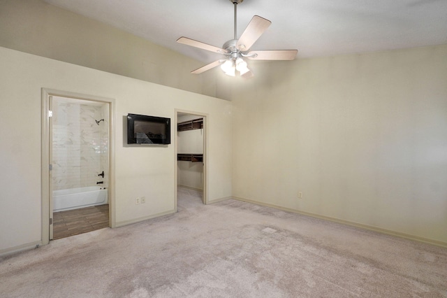 unfurnished bedroom featuring light carpet, a spacious closet, a closet, ensuite bathroom, and baseboards