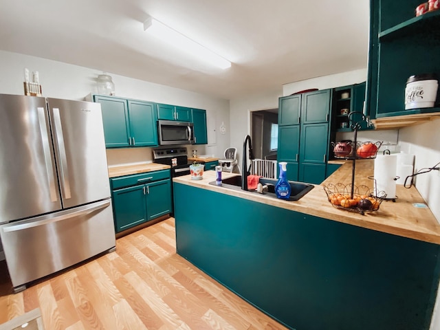 310 W Delta St, Aurora, MO 65605 - kitchen featuring appliances with stainless steel finishes, a peninsula, light wood finished floors, a sink, and green cabinets