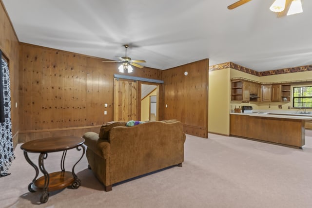 living room with a ceiling fan, wooden walls, and light colored carpet