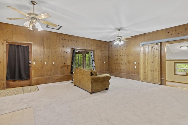 sitting room featuring a ceiling fan, wood walls, and carpet