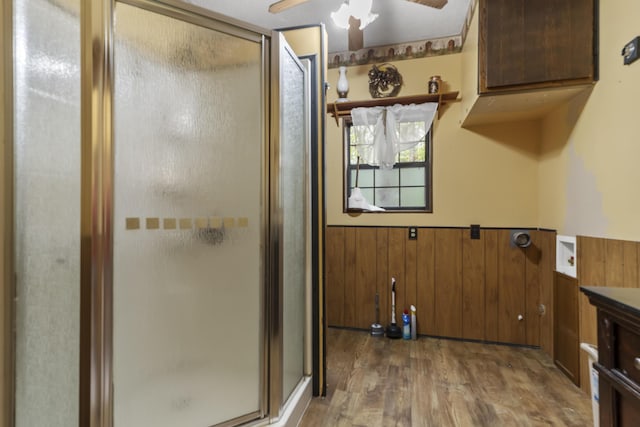 bathroom with wainscoting, wood finished floors, a shower stall, a ceiling fan, and wood walls