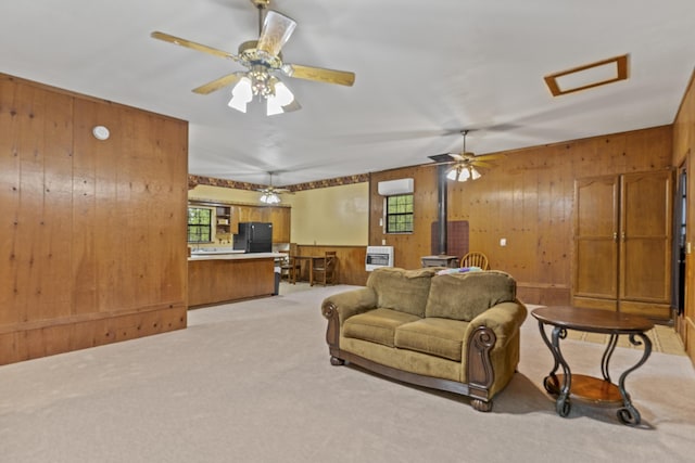 living area with light colored carpet, wooden walls, a wood stove, attic access, and a ceiling fan