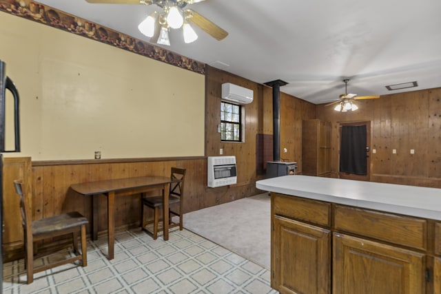 kitchen featuring wood walls, a wood stove, a ceiling fan, heating unit, and light floors