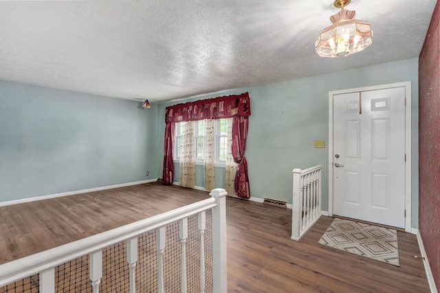 foyer with wood finished floors, a textured ceiling, baseboards, and a chandelier