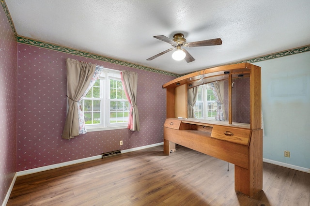 unfurnished office featuring wood finished floors, wallpapered walls, ceiling fan, a textured ceiling, and baseboards