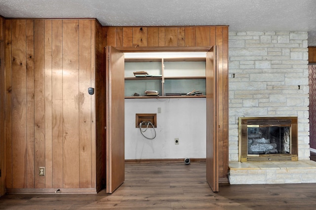 laundry view of a textured ceiling, wood finished floors, baseboards, wood walls, and a stone fireplace