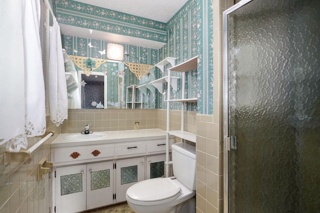 bathroom featuring wallpapered walls, tile walls, toilet, a shower stall, and vanity