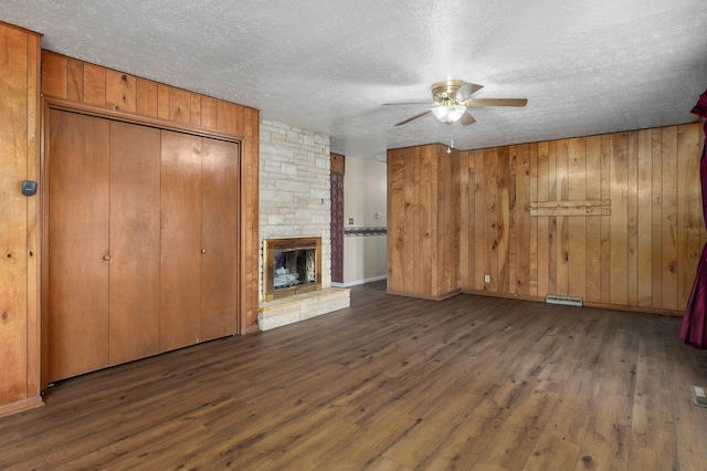unfurnished living room with ceiling fan, wood finished floors, a textured ceiling, wooden walls, and a fireplace