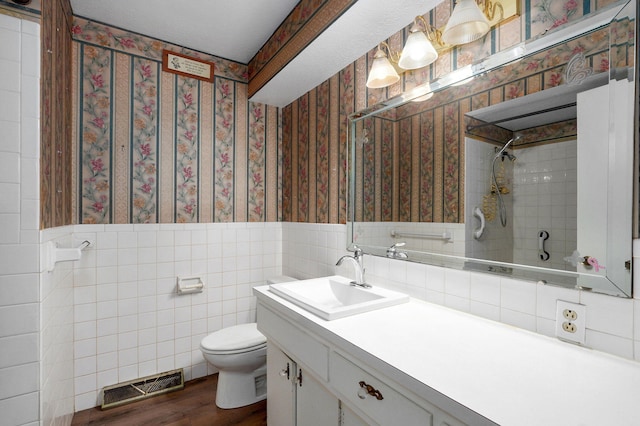 full bath featuring wallpapered walls, toilet, a wainscoted wall, a tile shower, and wood finished floors