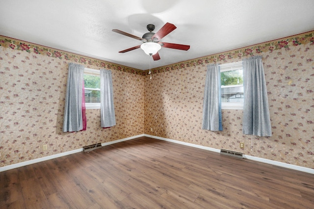 empty room with wood finished floors, baseboards, a ceiling fan, and wallpapered walls