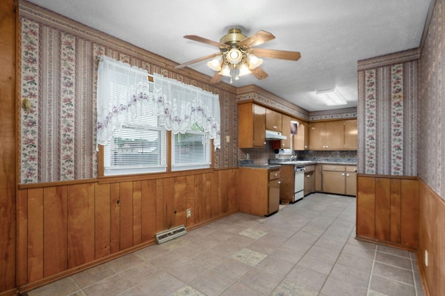 kitchen with under cabinet range hood, wainscoting, ceiling fan, brown cabinetry, and dishwasher