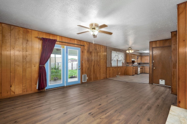 unfurnished living room featuring ceiling fan, wood finished floors, wood walls, and a textured ceiling