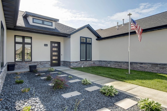 property entrance featuring stucco siding, stone siding, and roof with shingles